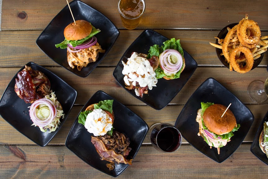 Four different types of grilled meat with vegetables, burger, onion rings, glass of red wine